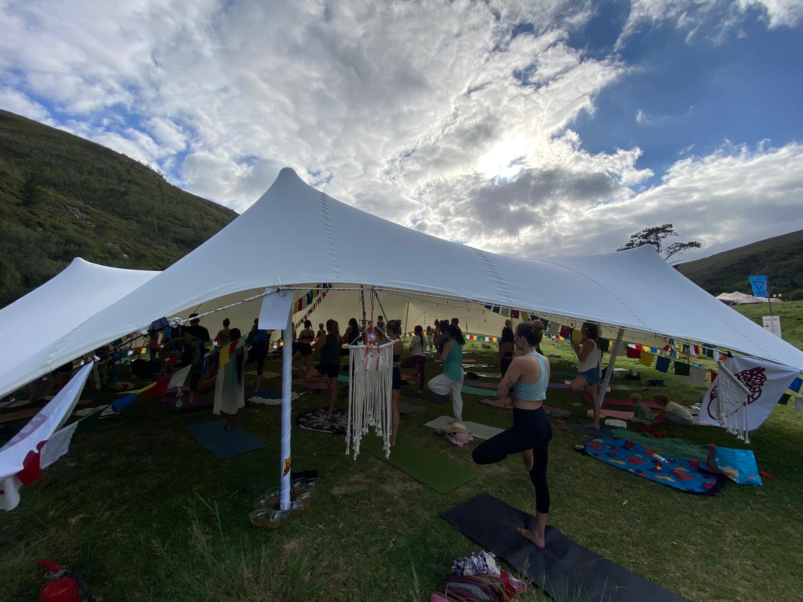 Outdoor yoga class in tree pose under a stretch tent in the mountains
