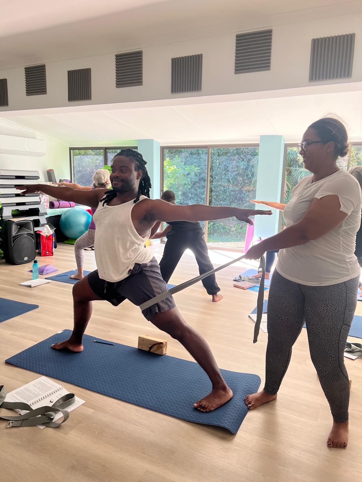 Student receiving a Warrior II strap assist during teacher training practice